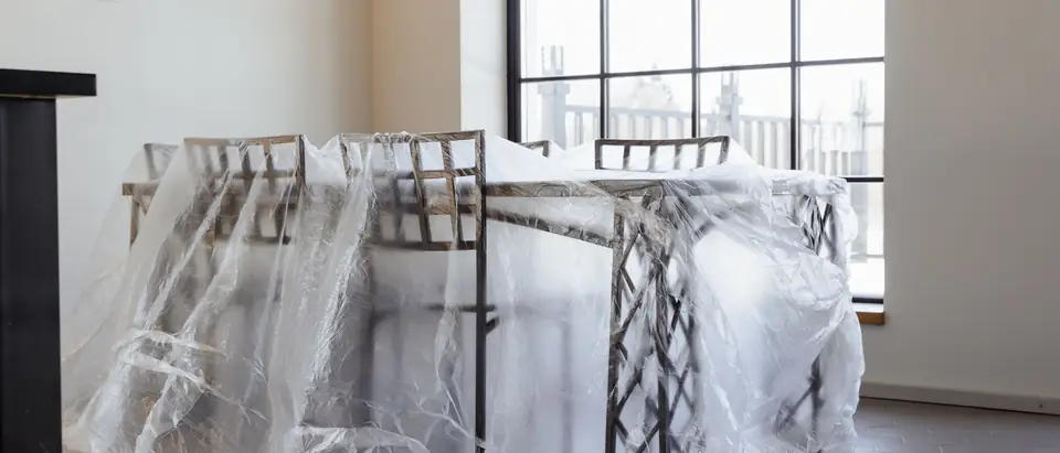 A table and chairs wrapped in clear plastic sheeting in a bright empty room