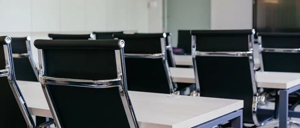 Rows of black office chairs at white desks in an empty room