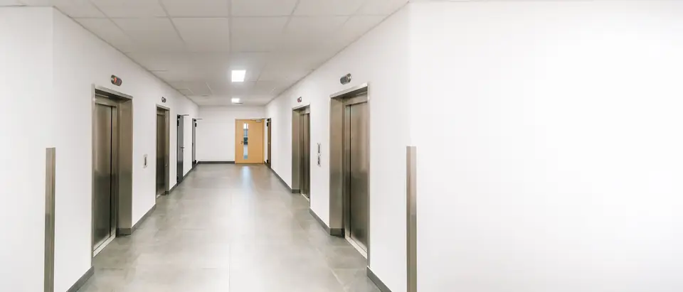 A bright office corridor with a row of stainless steel lift doors